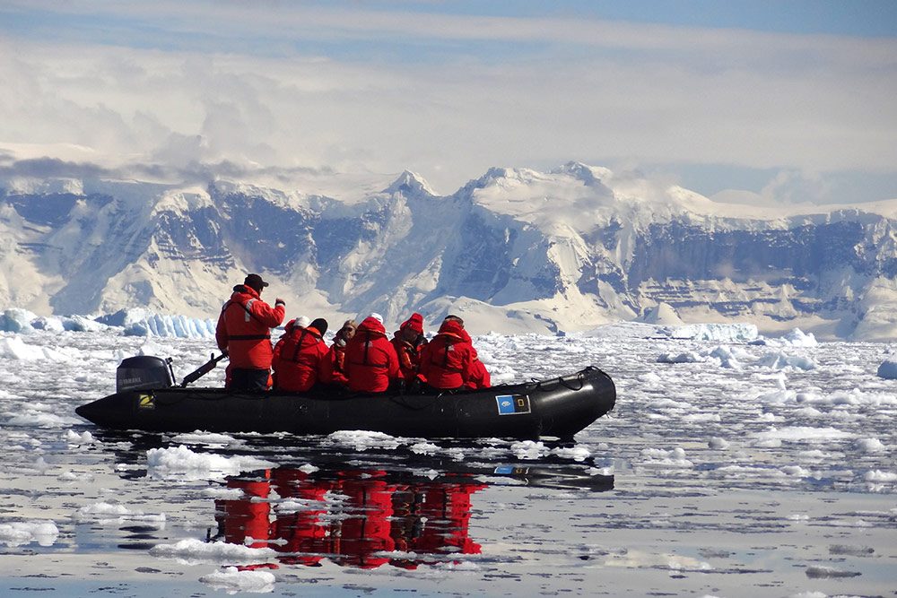 travelers in red winter coats rowing a zodiac boat amid floating ice and glaciers of Antarctica