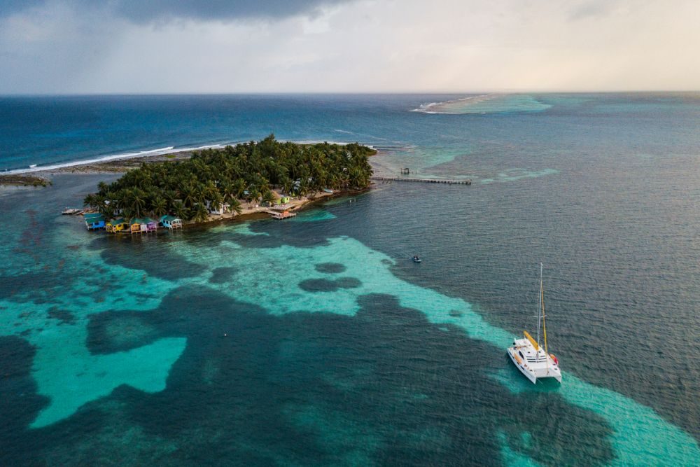 aerial photo of Tobacco Caye with sailboat and blue green ocean