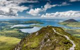 The hiking trail at the top of Diamond Hill in Connemara National Park, Ireland. Behind, the sun plays with the clouds reflected in the sea. - Image