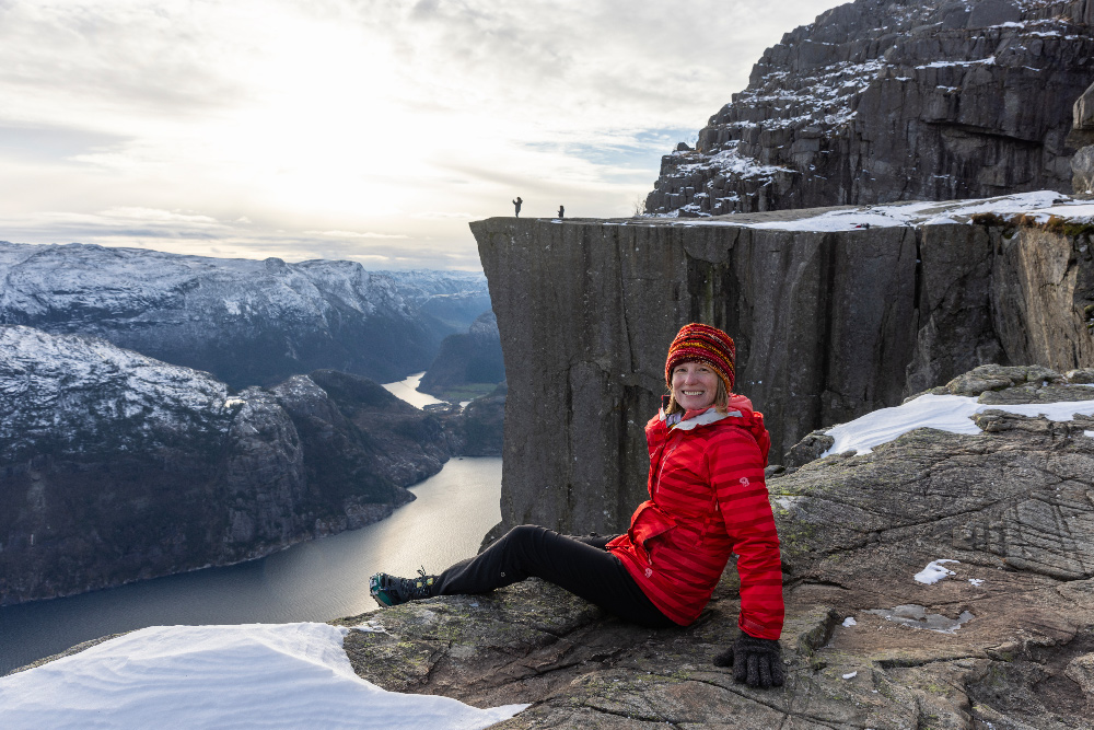 Brook posing in front of Pulpit Rock above Lysefjord with showy mountains in the background.