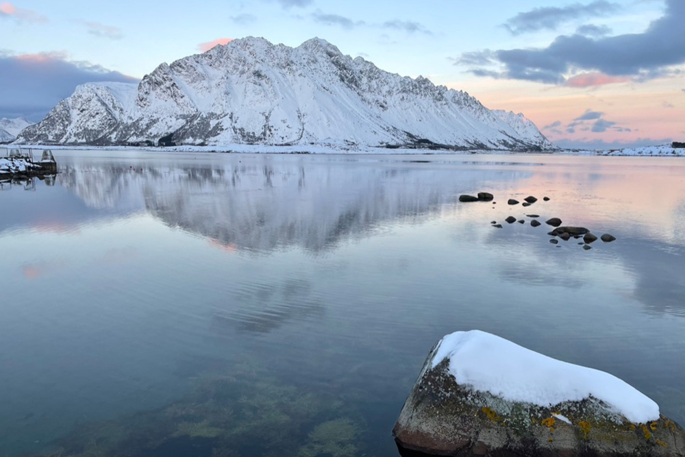 A landscape of the Lofoten Islands with snowy mountains and the Norwegian Sea.