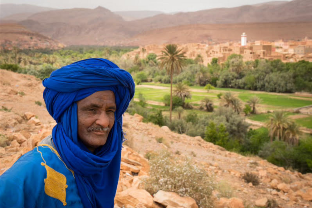 Moroccan man dressed in blue and yellow turban stands.