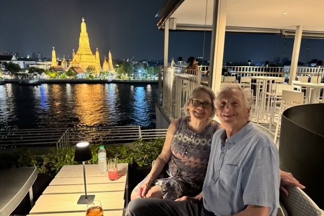 Tony Ford-Hutchinson and his wife Jane having a drink in Bangkok, with Wat Arun aglow in the background.