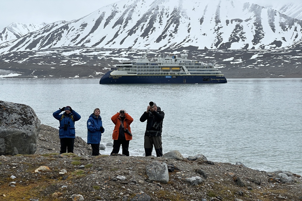 Passengers and a photography guide from the National Geographic Endurance in Spitsbergen capturing a group of short reindeer were hanging out on a steep grassy slope.
