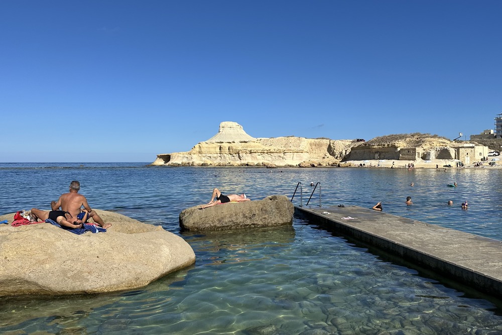 People swimming and sunbathing on the beach in Gozo, Malta.