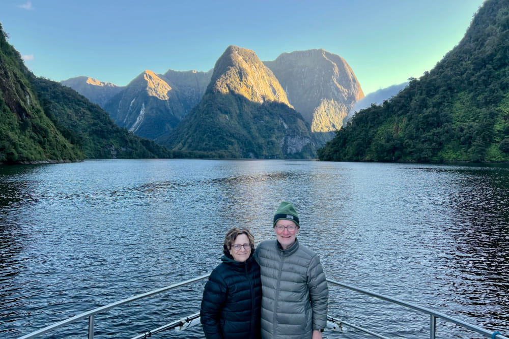 Karen Siegel and her partner on the deck as the morning sun hits the peaks above Doubtful Sound in Fiordland, New Zealand.