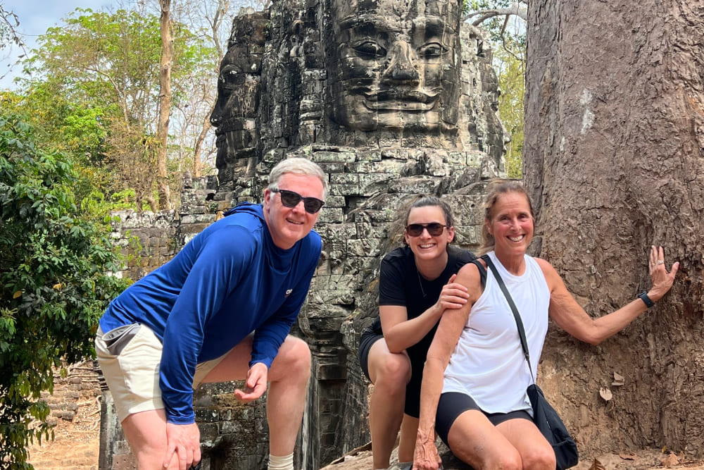 Liane Macmillan and family near a sculpted-face structure of Angor Wat, Cambodia.